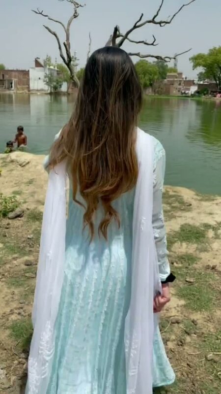 Roopsi Bansal from behind in a mint green embroidered kurta and white dupatta, standing quietly at the edge of a village pond