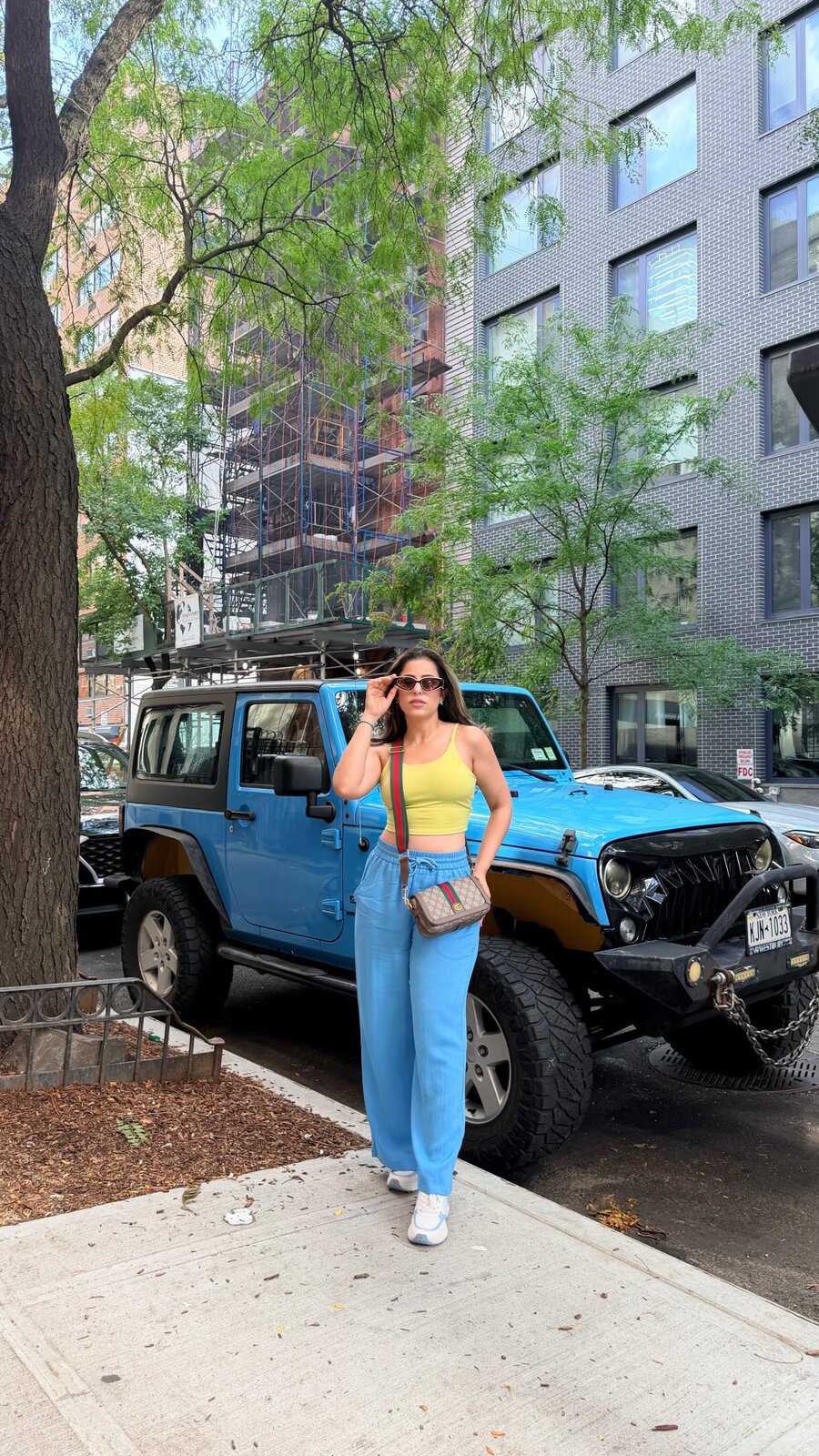 Roopsi Bansal in a yellow tank and powder blue Halara sweatpants on a New York City sidewalk next to a blue Jeep