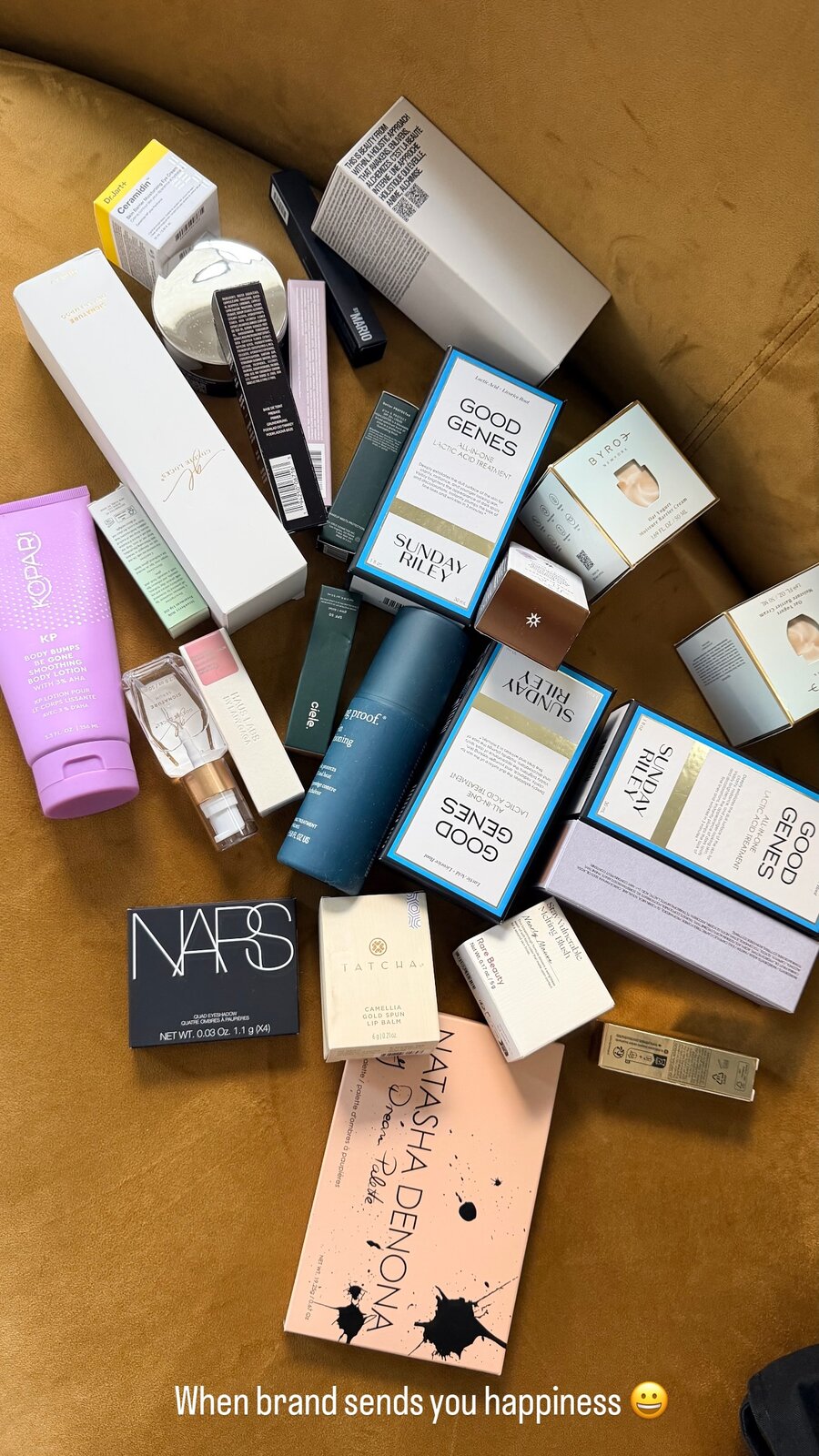 A flat lay of beauty PR boxes including Sunday Riley, NARS, Tatcha, and Natasha Denona spread across a mustard velvet couch