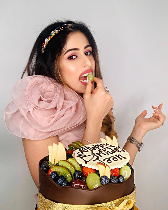 Biting into a grape from the fruit-topped birthday cake, mid-laugh, wearing the same jeweled headband