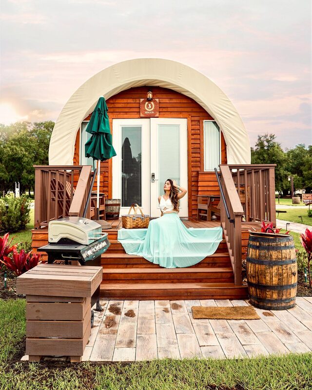 Roopsi Bansal in a white cutout top and mint green tulle skirt, seated on the porch steps of a round glamping cabin numbered three at Westgate River Ranch