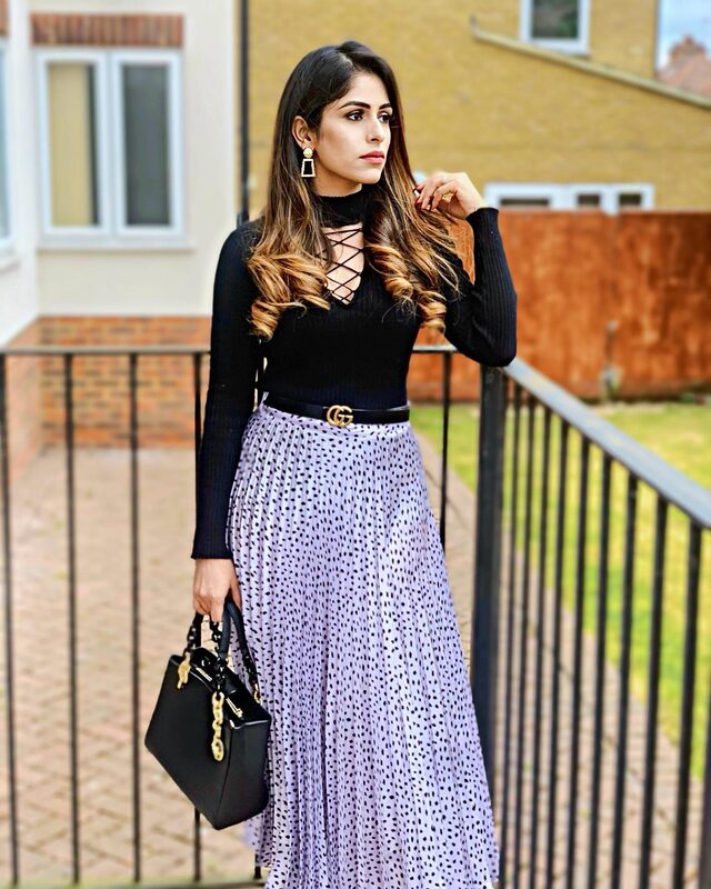 Walking down a brick side passage in a black lace-up top and a patterned midi skirt, carrying a black handbag