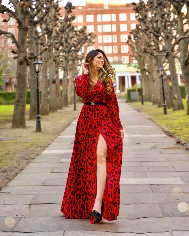 Roopsi Bansal in a red leopard-print wrap dress with a thigh-high slit and a black logo belt, walking down a tree-lined path
