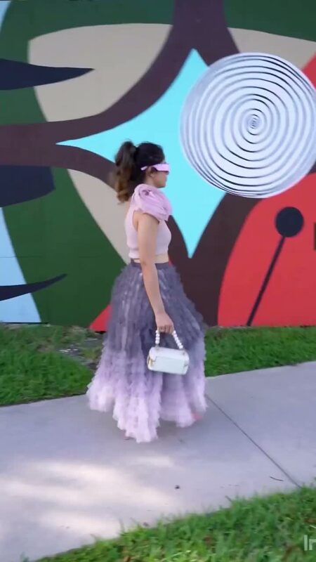 Roopsi Bansal in a pink top and ruffled lavender tulle skirt, walking past a surreal, candy-swirled abstract mural