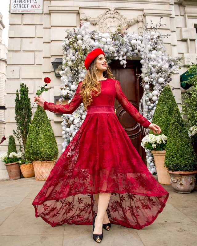 Roopsi Bansal in a red lace gown and red beret, holding a red rose in front of a wreath of white Christmas baubles on Henrietta Street