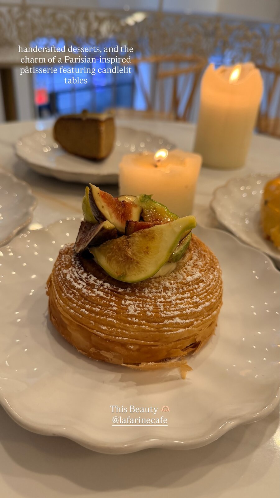 A fig-topped pastry dusted with powdered sugar on a plate at a candlelit table