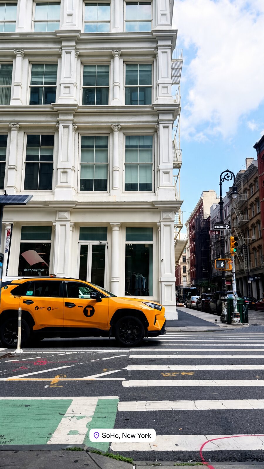 A yellow NYC taxi at a crosswalk in front of a cast-iron SoHo storefront
