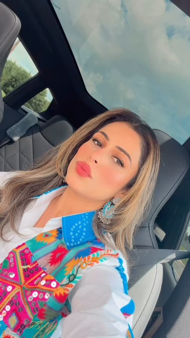 Roopsi Bansal in a car wearing a white shirt under a colorful mirror-work embroidered vest with turquoise peacock earrings
