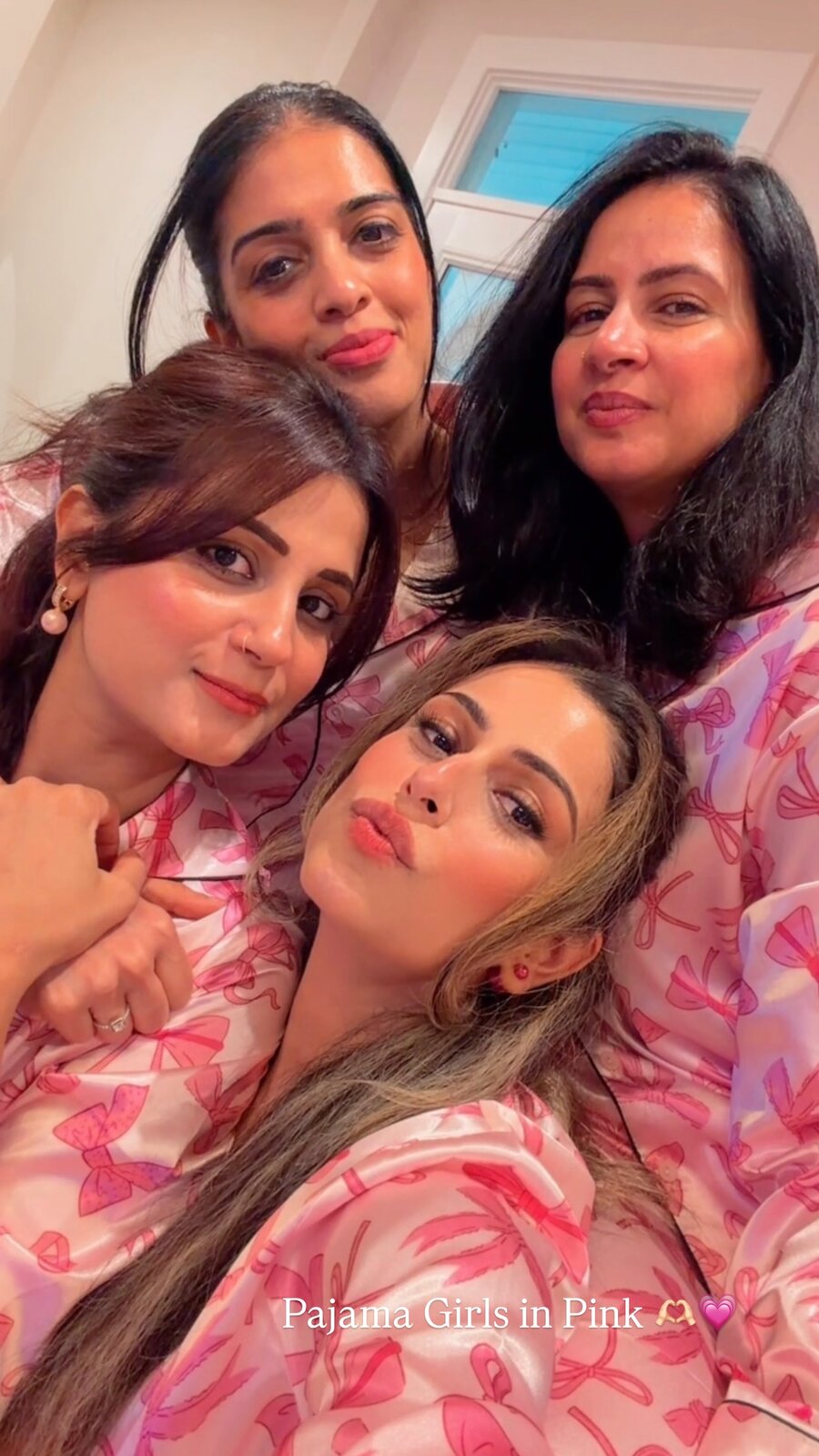 Roopsi Bansal and three friends piled together for a close-up selfie, all in matching pink bow-print pajamas, captioned 'Pajama Girls in Pink'