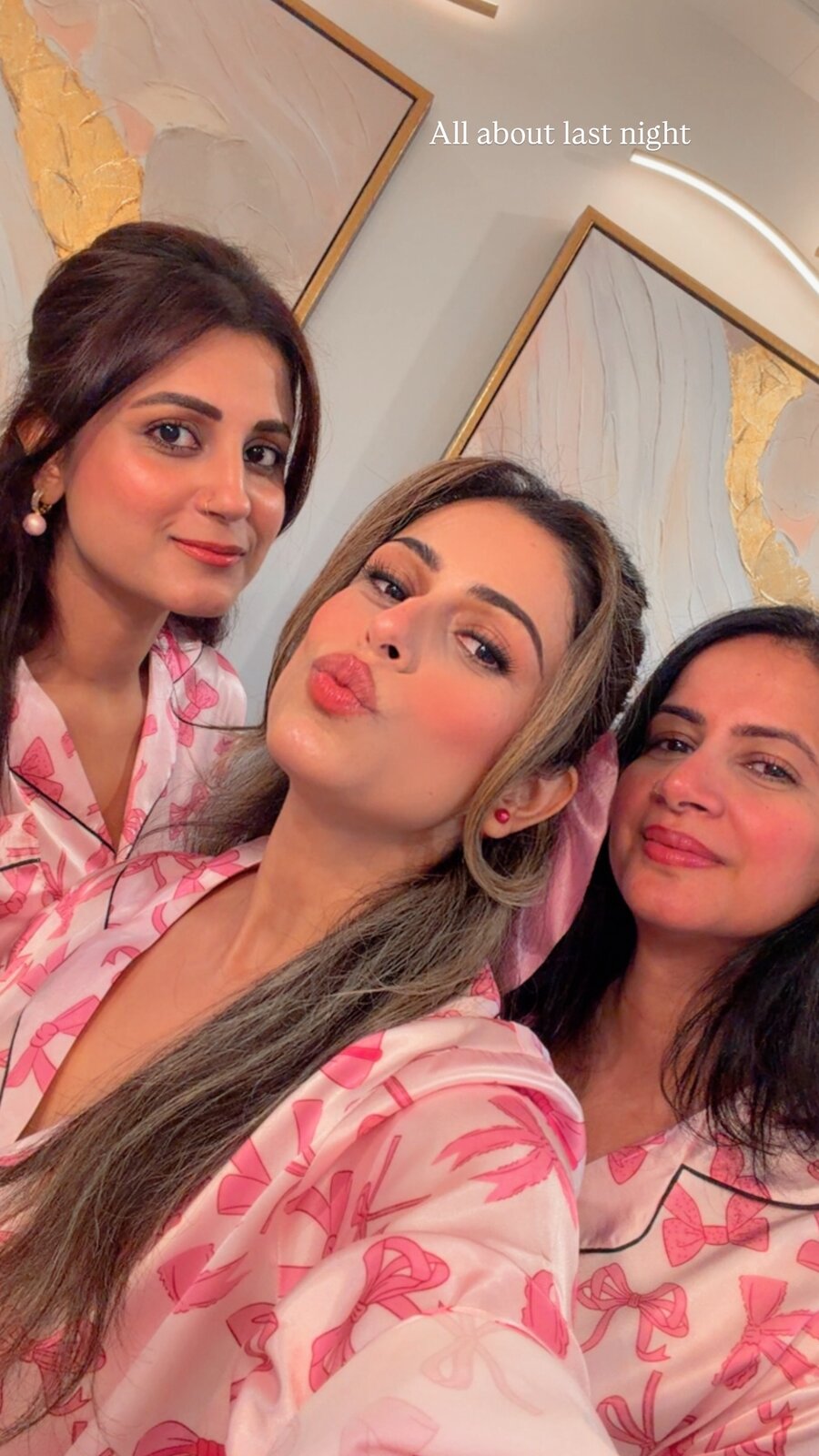 Roopsi Bansal and two friends taking a selfie together, all wearing matching pink bow-print pajama sets, captioned 'All about last night'