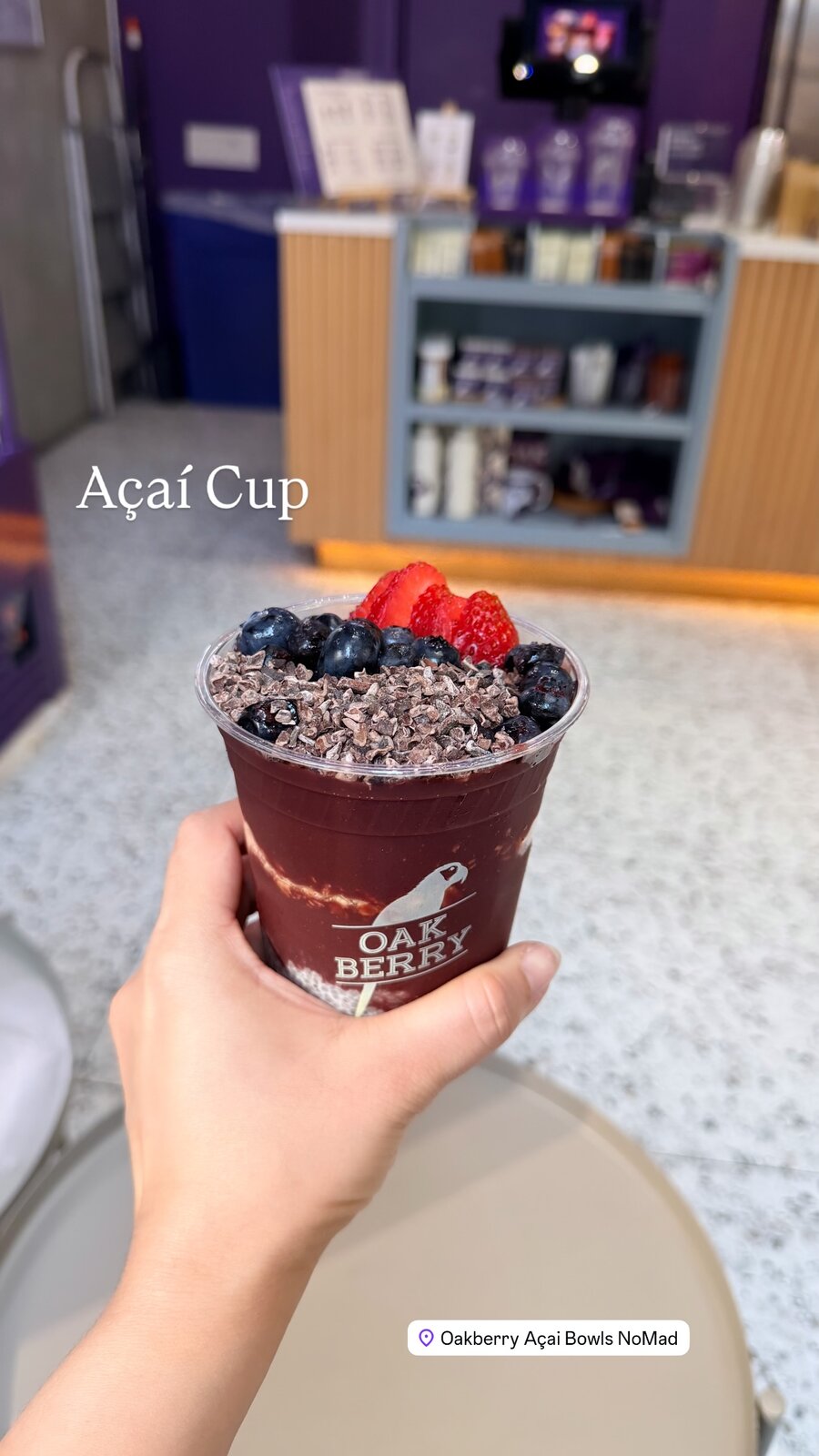 An açaí cup topped with blueberries, sliced strawberries, and cacao nibs, held up at Oakberry Açai Bowls in NoMad