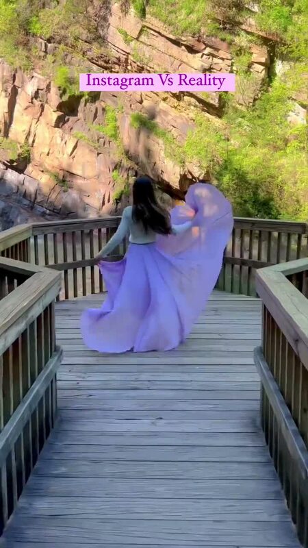 Roopsi Bansal in a white sweater and flowing lilac chiffon skirt from Chicwish, seen from behind twirling on a wooden overlook deck above a rocky Georgia gorge
