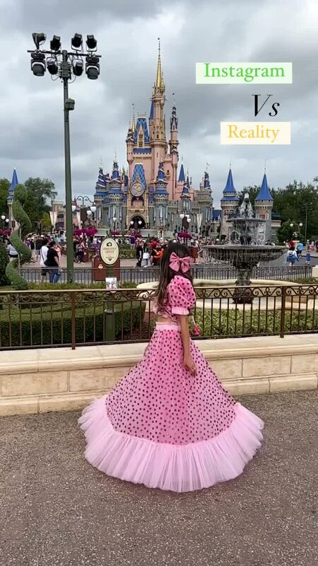 Roopsi Bansal in a pink polka-dot puff-sleeve tulle ball skirt with a pink bow, back to the camera, facing Cinderella Castle at Walt Disney World