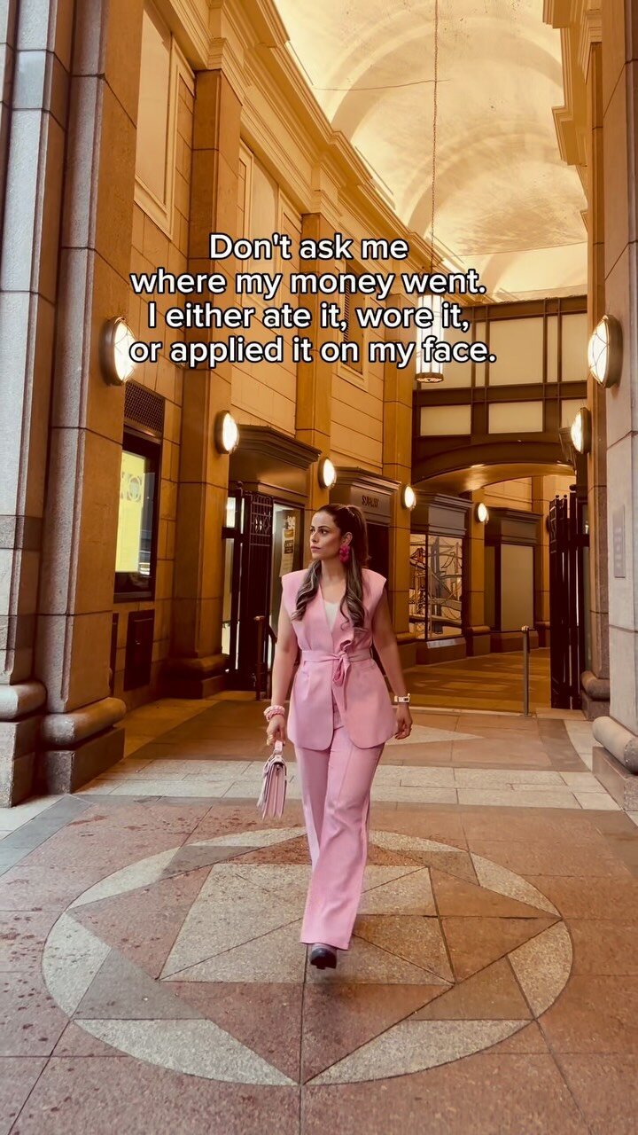 Roopsi Bansal in a pink sleeveless blazer co-ord walking through a colonnade