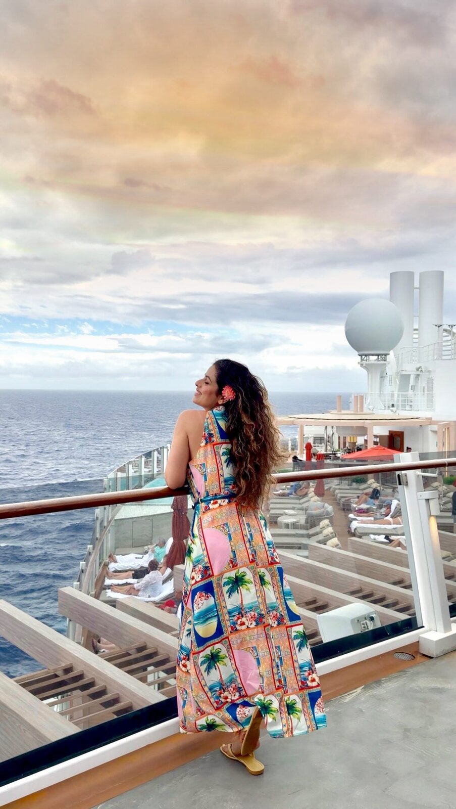 Roopsi Bansal in a palm-print maxi dress on a cruise ship deck at sunset
