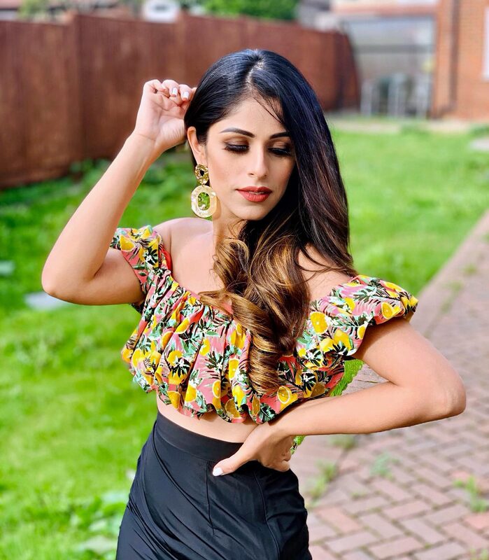 Roopsi Bansal in a tropical print off-shoulder crop top and statement earrings against a green fence backdrop