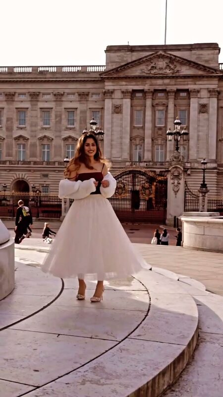 Roopsi Bansal in a cream faux-fur jacket and blush tulle skirt, twirling in front of Buckingham Palace at golden hour