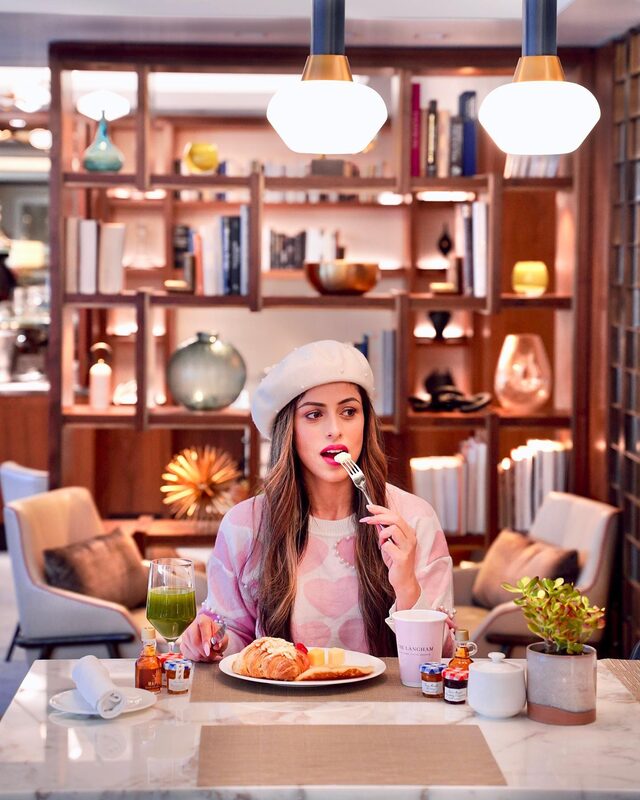 Roopsi Bansal in a pearl-embellished beret eating breakfast at a marble table in The Langham hotel lounge