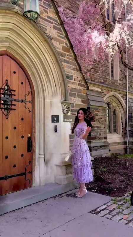 Roopsi Bansal in a lilac floral embroidered midi dress standing by a stone archway with cherry blossoms overhead