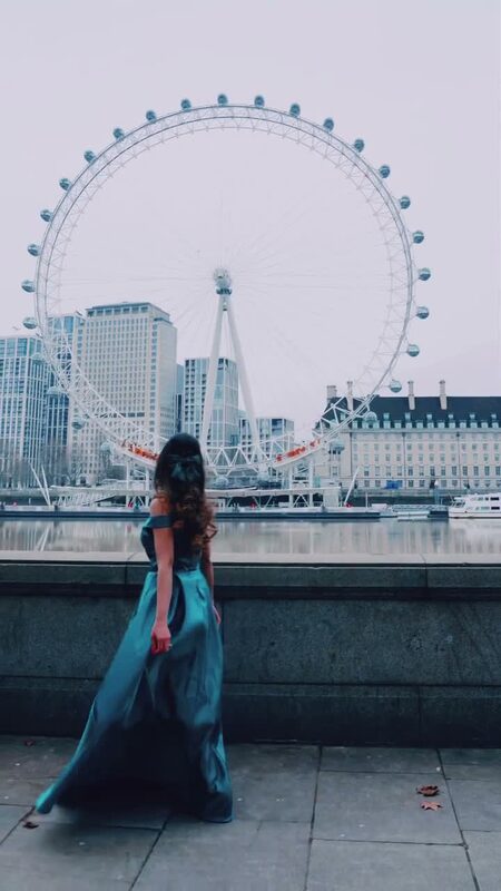 Roopsi Bansal from behind in a teal off-shoulder gown, facing the London Eye across the Thames