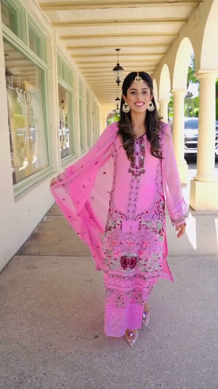 Roopsi Bansal in a pink embroidered Khas salwar kameez with a matching dupatta, jhumka earrings and a maang tikka, walking along a covered arcade