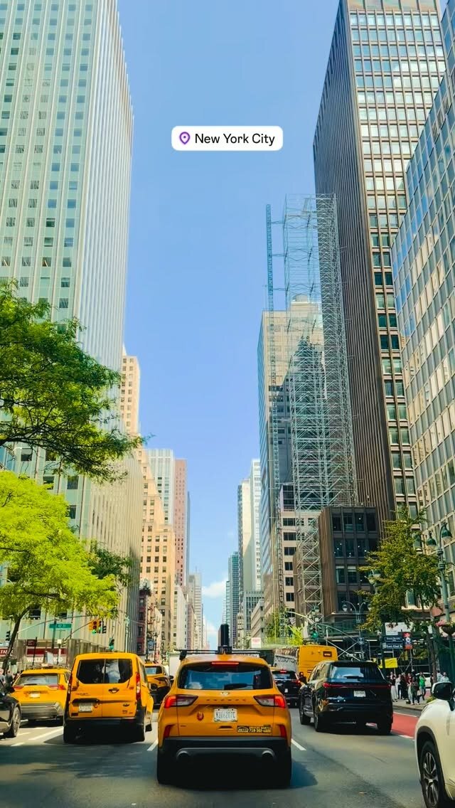 A New York City avenue full of yellow taxis under a clear blue sky, seen from inside a car