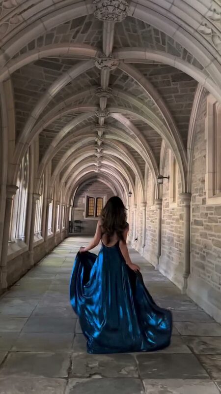 Roopsi Bansal trailing a metallic blue open-back gown through a vaulted Gothic cloister