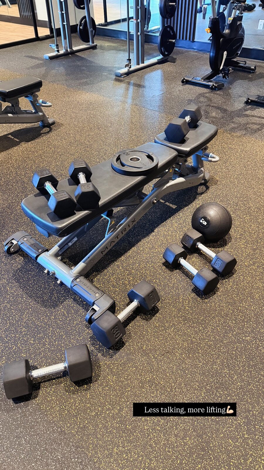 A gym floor with dumbbells, a weight bench, and a slam ball set up for a workout