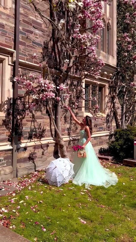 Roopsi Bansal in a mint tulle gown reaching up to touch magnolia blossoms next to a stone building at Princeton