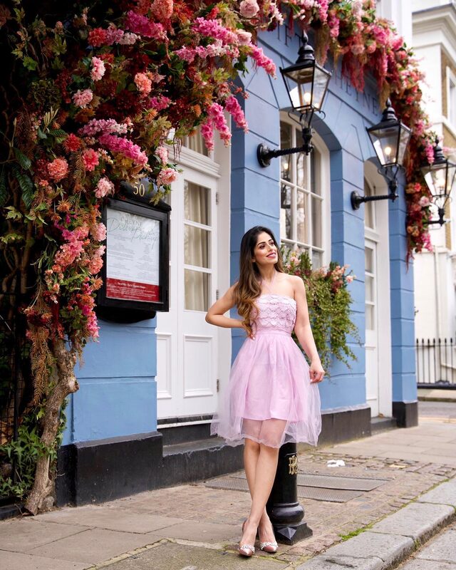 Roopsi Bansal in a pink lace-bodice tulle dress from Double Crazy Original, standing in front of the flower-covered facade of 50 Cheyne in London
