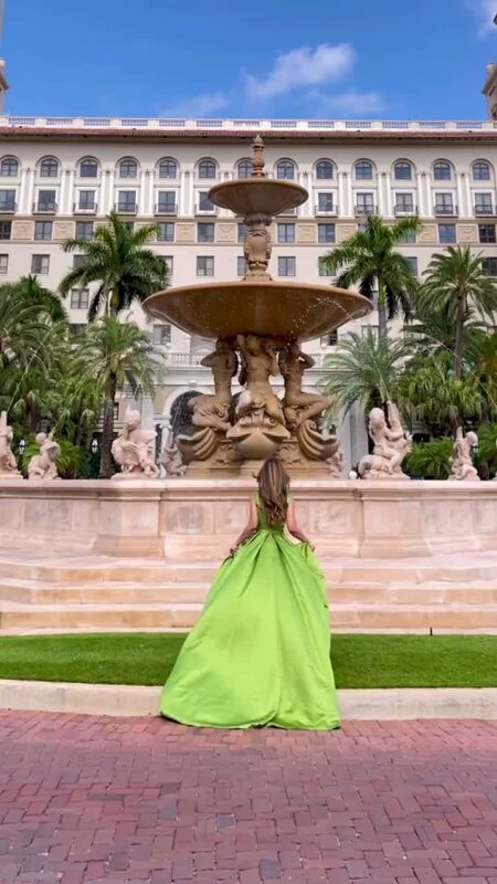 Roopsi Bansal in a bright green satin ballgown, back to the camera, facing the ornate tiered fountain at The Breakers in Florida