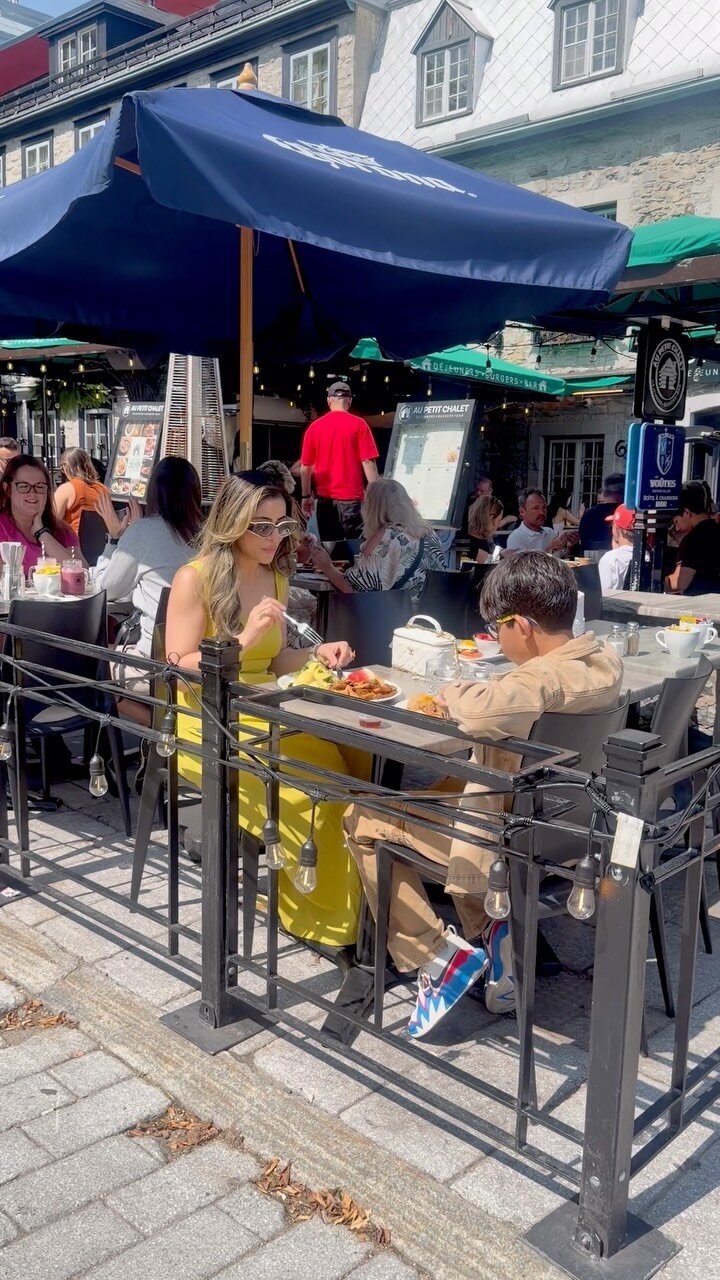 Roopsi Bansal in a yellow dress and sunglasses having lunch with her son at an outdoor café table in Old Québec City
