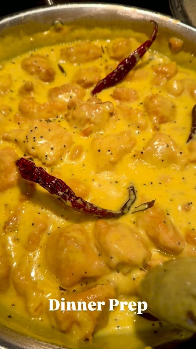 Creamy yellow curry with whole dried red chilies and mustard seeds simmering in a steel pan, captioned Dinner Prep