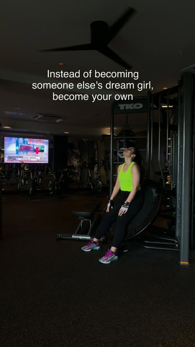 Roopsi Bansal in a neon green tank top and black leggings, leaning back against gym equipment mid-workout, with a caption reading Instead of becoming someone else's dream girl, become your own