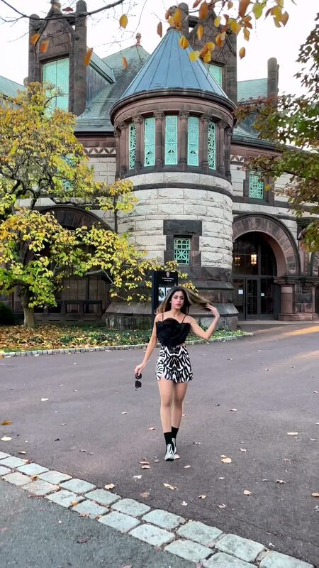 Roopsi Bansal in a black corset top and zebra-print skort standing in front of a Romanesque stone turret with stained-glass windows in Princeton, New Jersey