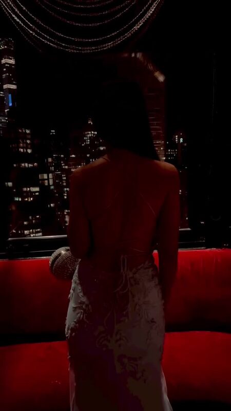 Roopsi Bansal in a backless white lace gown silhouetted against the New York City skyline at a cocktail party