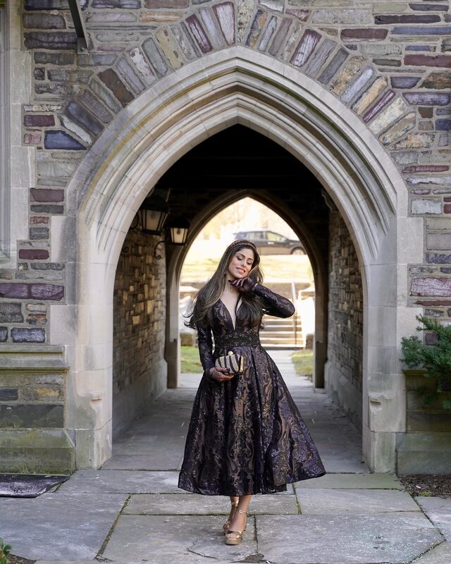 Roopsi Bansal in a black and gold brocade midi dress standing under a Gothic stone archway on Valentine's Day