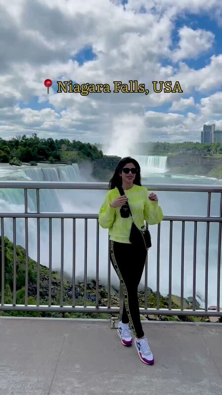 Roopsi Bansal in a neon yellow jacket at Niagara Falls, USA, with the falls and mist rising behind her