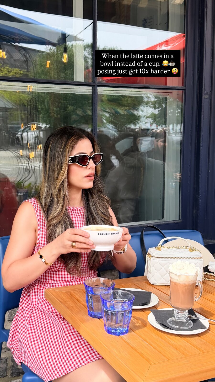 Roopsi Bansal holding a latte served in a wide white bowl branded Cochon Dingue, seated at an outdoor table