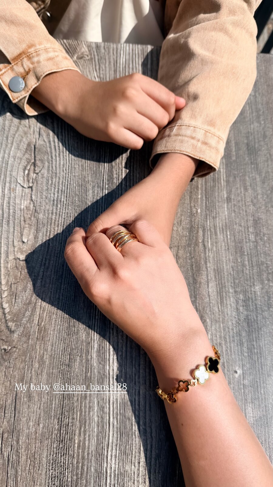 Roopsi Bansal holding her son Ahaan's hand on a wooden table, wearing a gold clover bracelet and rings