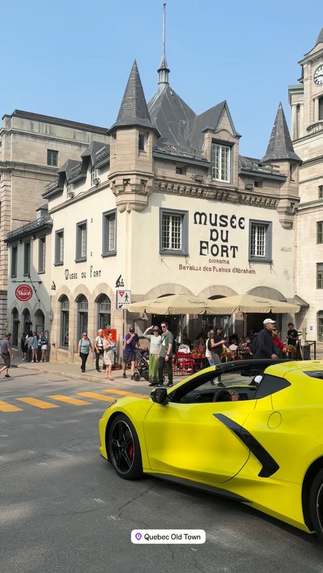 A yellow convertible sports car driving past the Musee du Fort building in Quebec Old Town, with tourists on the sidewalk
