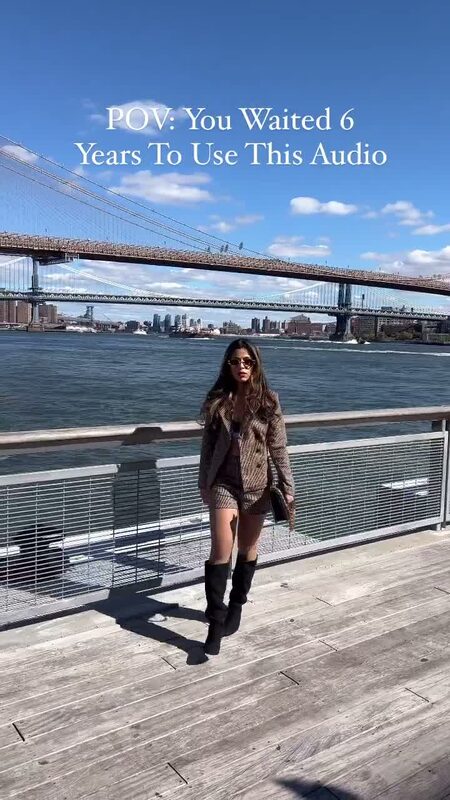 Roopsi Bansal in a houndstooth blazer and shorts set on the Seaport pier, Brooklyn and Manhattan Bridges behind her