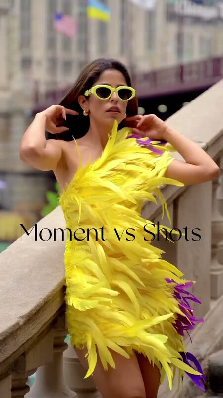 Roopsi Bansal in a yellow and purple feather mini dress and retro cat-eye sunglasses, leaning against a stone railing with the on-screen text Moment vs Shots