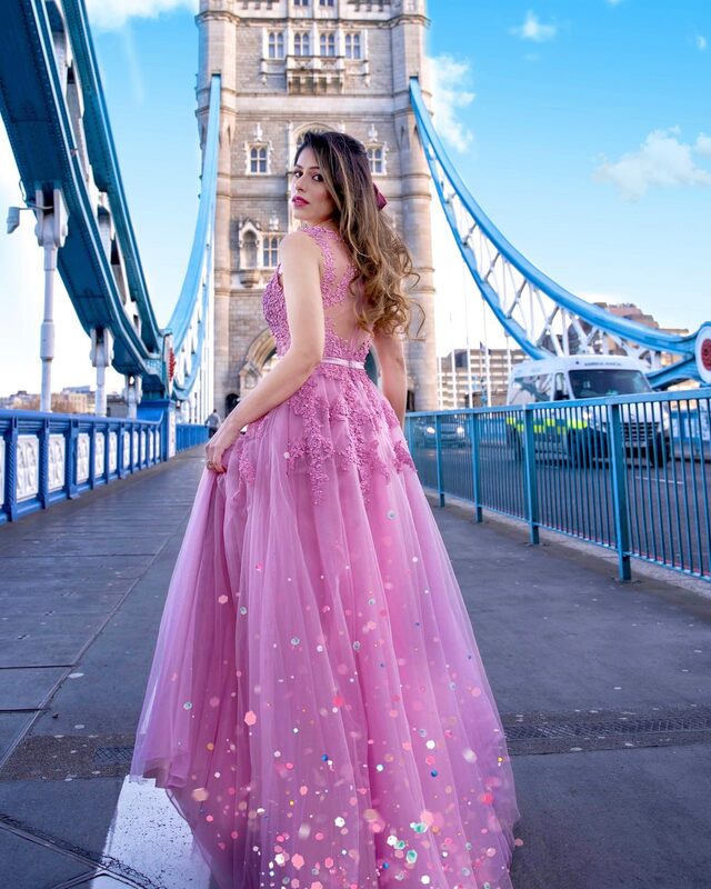 Roopsi Bansal in a pink tulle princess dress with beaded floral appliqué, looking back over her shoulder on Tower Bridge