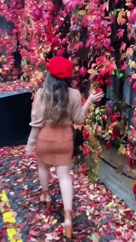 Roopsi Bansal from behind in a red beret and camel mini skirt, reaching toward a wall completely covered in deep red autumn ivy