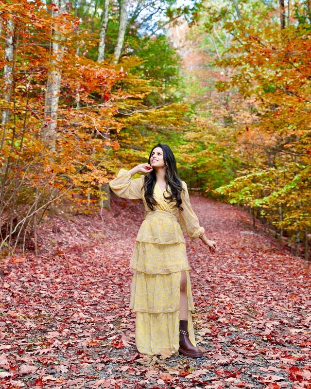 Roopsi Bansal in a yellow floral tiered maxi dress from Shein walking a leaf-covered forest path in the Catskills, New York