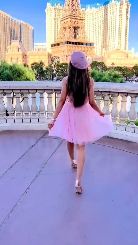 Roopsi Bansal from behind in a pink tulle skirt and mauve beret, walking across a bridge with the Paris Las Vegas replica Eiffel Tower rising behind her
