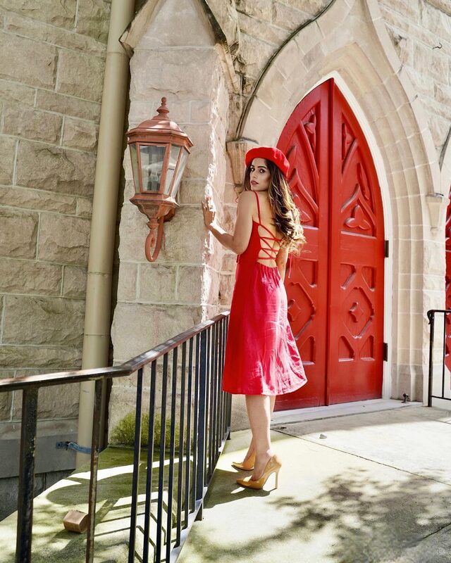 Roopsi Bansal in a red lace-up back dress and red beret, standing beside a large red Gothic church door in Jacksonville, Florida