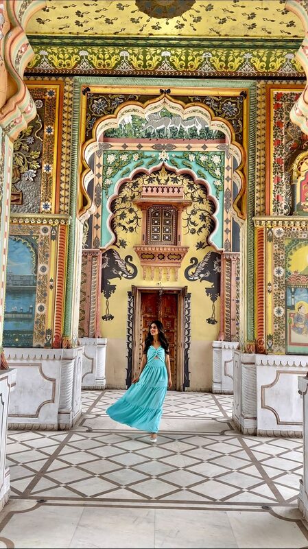 Roopsi Bansal in a turquoise dress standing beneath an intricately painted archway with elephant murals at Patrika Gate, Jaipur