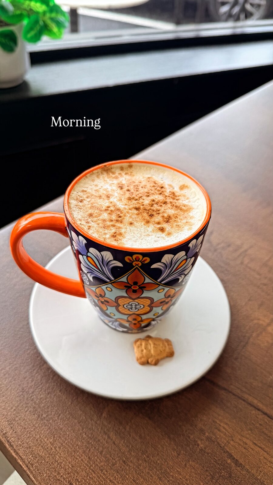 A cappuccino dusted with cinnamon in a colorful painted mug on a saucer